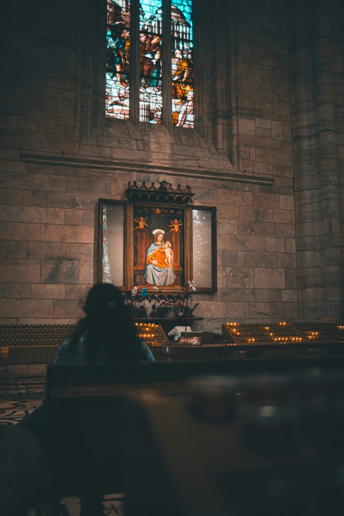 A person sitting in quiet reflection near a stained-glass window, symbolizing inner healing, spiritual rest, and the presence of Christ in suffering.